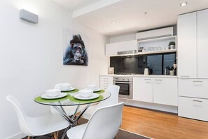 Una cucina moderna con mobili bianchi, un piano cottura in acciaio inox e una zona pranzo con sedie bianche e un tavolo in vetro.
