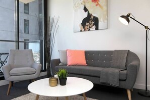 Una sala de estar moderna con un sofá gris, una mesa de centro blanca, un sillón gris, una lámpara de pie y un ventanal grande.