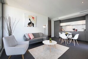 Una sala de estar moderna con un sofá gris, un sillón blanco, una mesa redonda de centro y un comedor con sillas blancas.