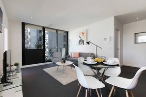 A modern living room with a sofa, a dining table with chairs, a TV, and a large window.