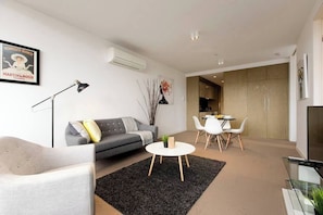 A modern living room with a grey sofa, a round coffee table, and a dining area with white chairs.