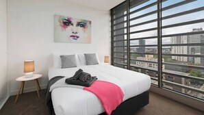 A modern hotel room with a large bed, a city view, a painting on the wall, and a small bedside table with a lamp. - HUGO - Live the good life *Wifi GYM Parking Views (Melbourne)
