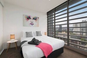 Una moderna camera d'hotel con un letto grande, vista sulla città, un quadro appeso e un comodino con una lampada.