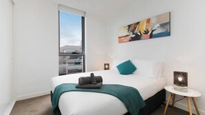 A modern hotel room with a large bed, a window, a painting on the wall, and a bedside lamp. - HUGO - Live the good life *Wifi GYM Parking Views (Melbourne)
