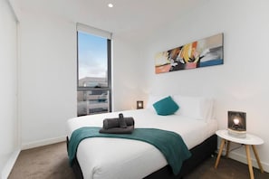 A modern hotel room with a large bed, a window, a painting on the wall, and a bedside lamp.