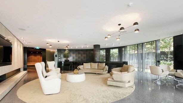 A spacious lobby with a modern design, featuring a curved sofa, white armchairs, a round coffee table, and a large TV screen. - HUGO - Live the good life *Wifi GYM Parking Views (Melbourne)