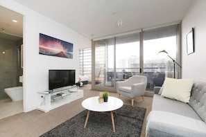 Un soggiorno moderno con una TV a schermo piatto, un tavolino rotondo, un divano grigio e un'ampia finestra con vista sulla città.
