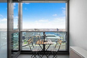 A balcony with a table and chairs, overlooking a cityscape with modern buildings and a bridge.
