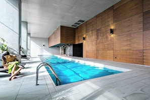An indoor swimming pool with a tiled floor, wooden panel walls, and a person by the pool.
