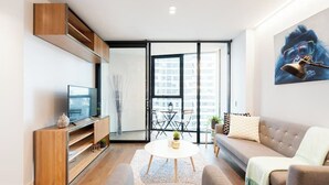 A modern living room with a TV, sofa, coffee table, and a large window with a city view. - Stunning Apartment Close to Queen Victoria Markets (Melbourne)