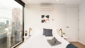 A modern hotel room with a large bed, two bedside tables with lamps, a city view, and a door. - Stunning Apartment Close to Queen Victoria Markets (Melbourne)
