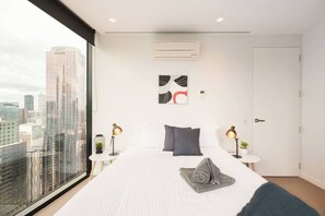 A modern hotel room with a large bed, two bedside tables with lamps, a city view, and a door.