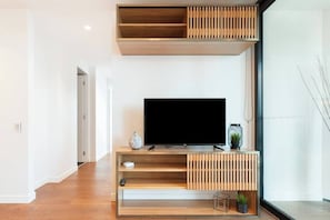 A modern living room with a flat-screen TV, wooden shelves, and a glass door leading to a balcony.