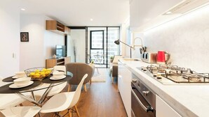 A modern kitchen with a gas stove, dining area with chairs and a table, and a view through a glass door to the living area. - Stunning Apartment Close to Queen Victoria Markets (Melbourne)