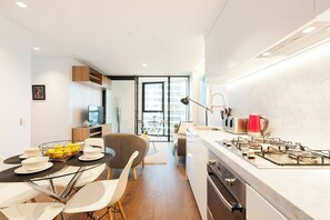A modern kitchen with a gas stove, dining area with chairs and a table, and a view through a glass door to the living area.