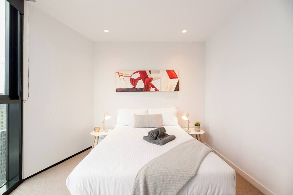 Una habitación de hotel moderna con una cama grande, un cuadro encima y una ventana a la izquierda.