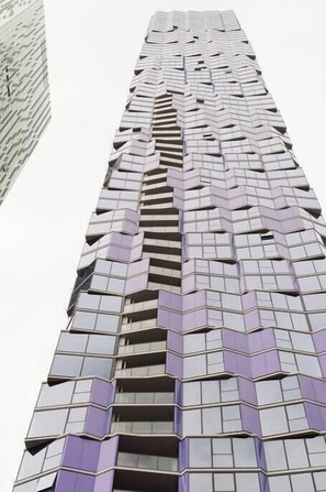 Een hoog gebouw met een opvallend zigzagpatroon, meerdere balkons en een modern architectonisch ontwerp.