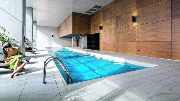 An indoor swimming pool with a tiled floor, a wooden wall, and a person near the pool. - Phoenix - Amazing Location with Gym Sauna Pool Internet (Melbourne)