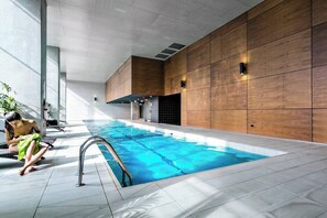 An indoor swimming pool with a tiled floor, wooden panel walls, and a person by the pool.