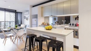 A modern kitchen with a central island, bar stools, and a dining area with a glass table and chairs.