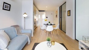 A modern living room with a sofa, a dining table with chairs, and a kitchen in the background.