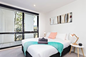 Una camera da letto moderna con un'ampia finestra, un letto con una coperta color petrolio, un quadro e una lampada da comodino.
