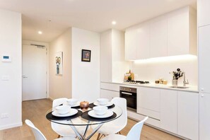 A modern kitchen with white cabinets, a glass dining table, and white chairs.