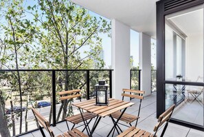 Un balcone con tavolo e sedie in legno, una lanterna e vista su alberi ed edifici.