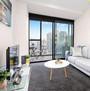 A modern living room with a glass coffee table, a white sofa, and a large window with a city view.