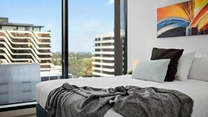Una habitación de hotel moderna con una cama grande, vistas a edificios y un cuadro en la pared.