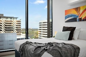 Una camera d'albergo moderna con un letto grande, vista sulla città e un quadro colorato al muro.