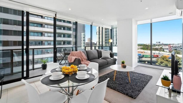A modern apartment with a balcony, a dining area, a sofa, and a TV.
