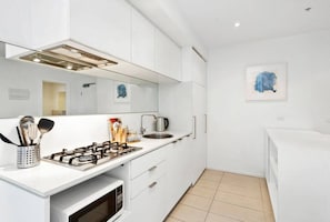 A modern kitchen with white cabinetry, a gas stove, a microwave, and a sink.