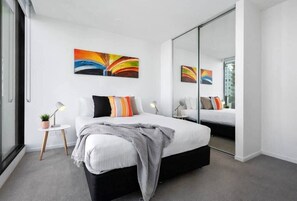 Ein modernes Schlafzimmer mit einem Bett, Nachttischen, einem Spiegel und einem farbenfrohen abstrakten Gemälde.