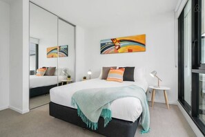 Une chambre à coucher moderne avec un grand lit, des tables de chevet, un miroir et des œuvres d’art accrochées au mur.