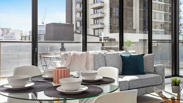 A modern living room with a glass table, white sofa, and a city view.