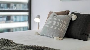 A bed with two pillows, a lamp, and a window with a view of buildings.