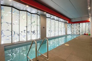 A swimming pool with a glass barrier, a metal ladder, and a red ceiling.