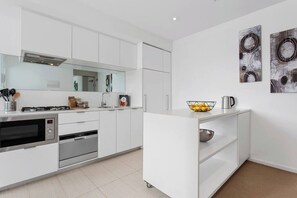 A modern kitchen with white cabinetry, stainless steel appliances, and a small island with a bowl and kettle.