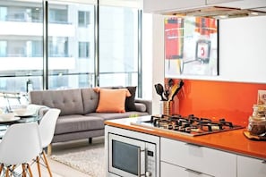 Una cucina moderna con piano cottura a gas, forno a microonde e zona pranzo con divano grigio e sedie bianche.