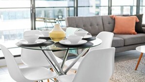 Ein moderner Essbereich mit einem Glastisch, weißen Stühlen und einem grauen Sofa mit einem Pfirsichkissen.