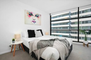 Una camera da letto moderna con un letto grande, una finestra vista città, un comodino e un'opera d'arte appesa al muro.