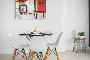 A dining area with a round table, white chairs, and a painting on the wall.
