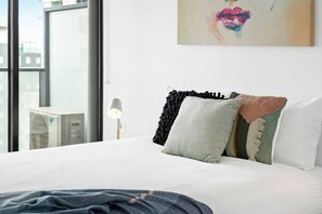 Habitación de hotel con una cama grande, ventana con vista a edificios y un cuadro en la pared.