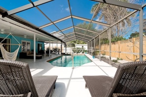 A covered outdoor swimming pool with wicker chairs and a hammock.