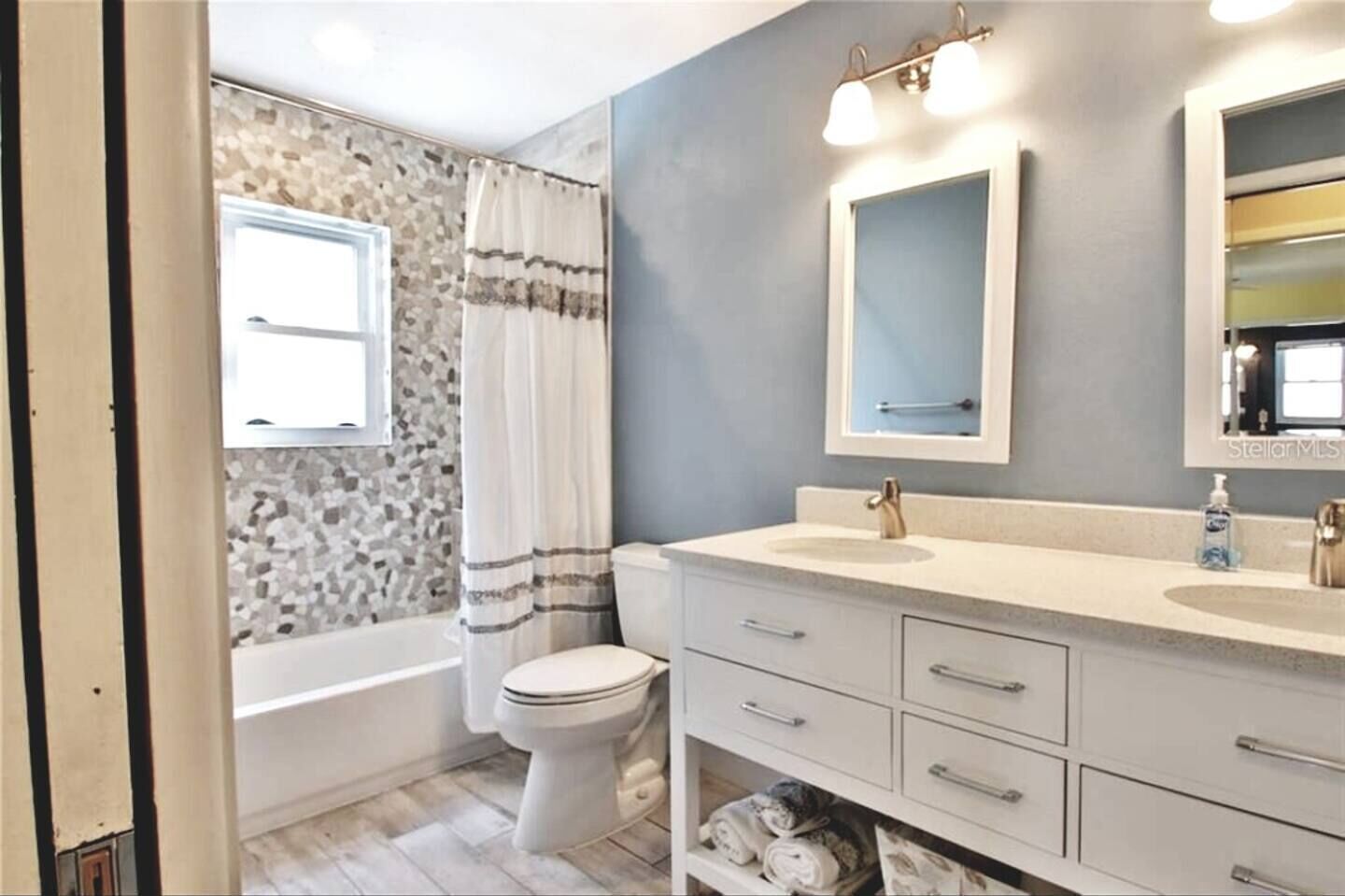 Une salle de bain avec un mur décoré de mosaïques, une baignoire, des toilettes, un meuble-lavabo avec un évier et un miroir.