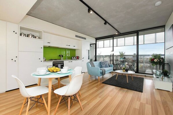 A modern apartment with a dining area, kitchen, and living space with large windows.