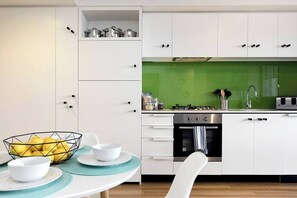 A modern kitchen with white cabinets, a green backsplash, and a dining area with a table set for two.