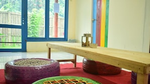 Una habitación con un ventanal grande, una mesa de madera y alfombras de juego de colores en el suelo.