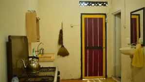 Cocina compacta con estufa a gas, lavamanos y una escoba colgada en la pared.